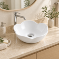 Lavamanos blanco con borde en forma de flor instalado sobre mesón de baño; grifería cromada de ambientación.
